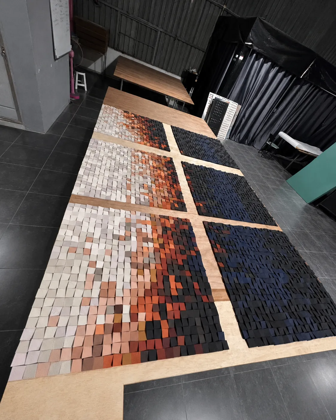 Large wood mosaic panels laid out flat on a workshop floor, a sunrise gradient running from pale grey through orange into deep navy